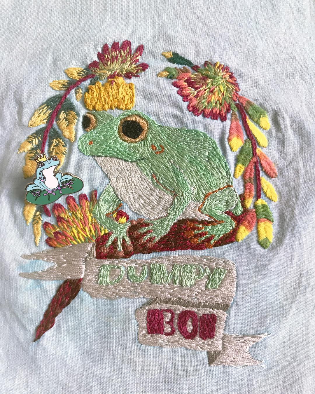 Embroidery of a tree frog around leaves and on a tree branch, with a banner below that reads 'Dumpy Boi' 